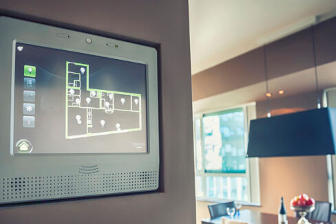 Wandmontiertes Smart-Home-Display zeigt den Grundriss einer Wohnung mit vernetzten Geräten und Lichtsteuerung in einem modernen Wohnraum. | Immobilienbewertung